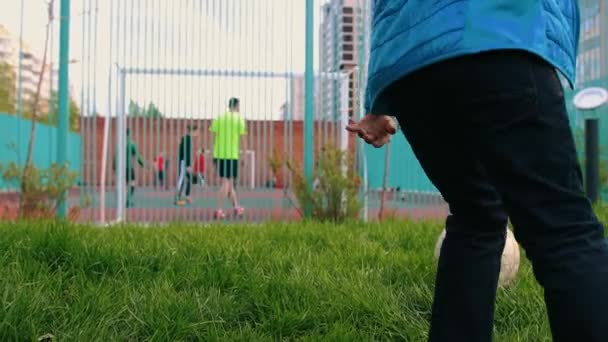 Un niño pequeño caminando hacia el patio de fútbol y cayendo sobre la hierba — Vídeo de stock