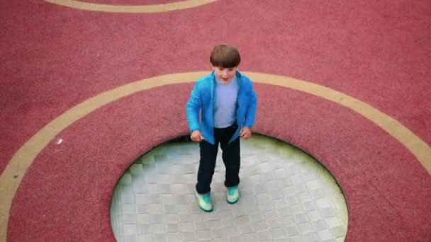 Un niño saltando en el trampolín en el patio de recreo — Vídeos de Stock