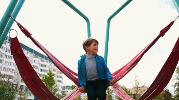 Um rapazinho a balançar nos baloiços do parque infantil — Vídeo de Stock