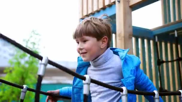 Ein kleiner Junge läuft auf der Hängebrücke auf dem Spielplatz — Stockvideo