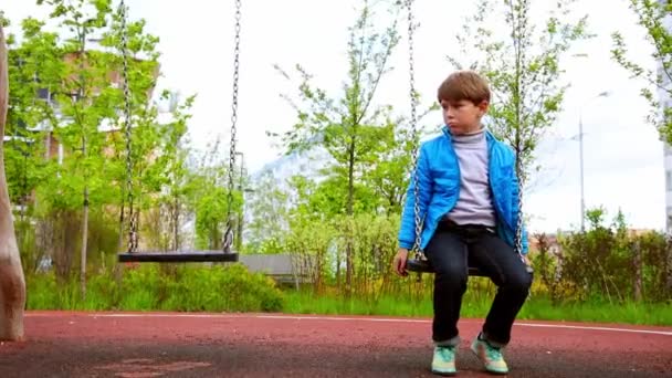 Un petit garçon triste assis sur les balançoires — Video