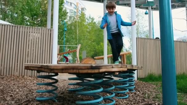 Ein kleiner Junge spielt auf dem Spielplatz im Freien - er springt auf den Ständer an der Quelle — Stockvideo