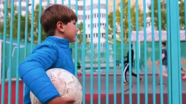 Un niño pequeño sosteniendo la pelota de fútbol y caminando por el patio de recreo — Vídeos de Stock