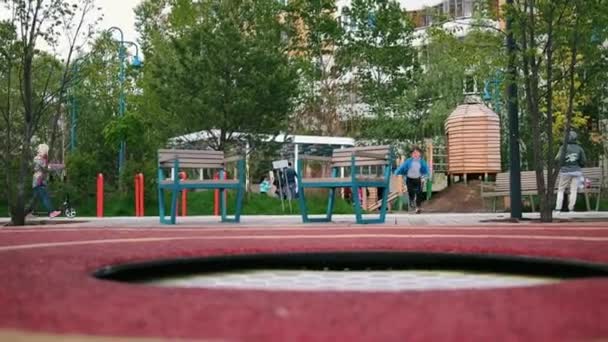 Een kleine jongen springt op de trampoline op de buitenspeelplaats — Stockvideo