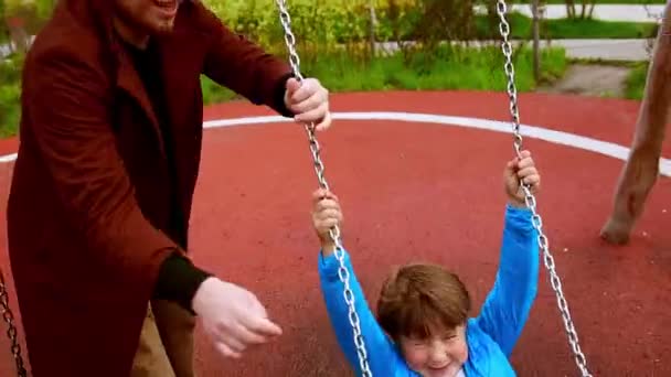 Jovem balançando seu irmãozinho feliz nos balanços no playground — Vídeo de Stock