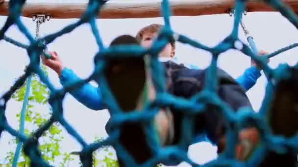 Een kleine jongen zwaait op de afgeronde schommels op de speelplaats van de kinderen — Stockvideo