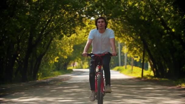 Junger Mann im weißen Hemd fährt Fahrrad und trinkt Wasser — Stockvideo