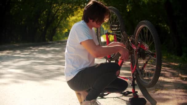 Jovem consertando sua bicicleta no parque — Vídeo de Stock