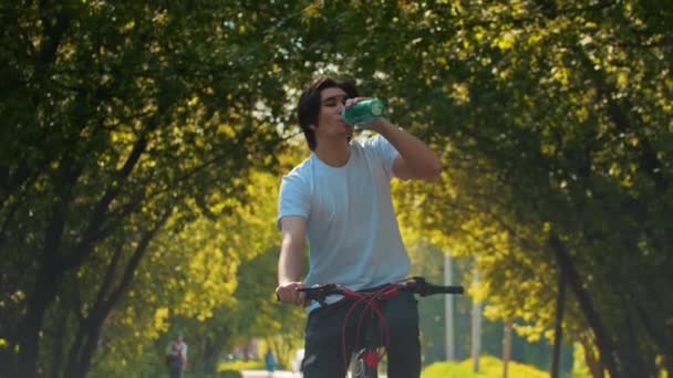 Jovem homem esportivo andando de bicicleta e beber água da garrafa — Vídeo de Stock