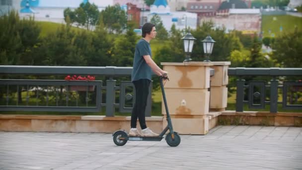 Jovem homem bonito montando uma scooter elétrica na área quadrada — Vídeo de Stock