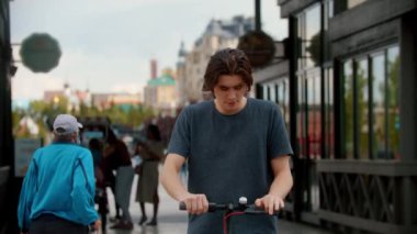 Yoğun bir caddede elektrikli scooter kullanan genç bir adam duruyor ve telefonla konuşuyor.