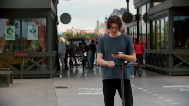 Jovem falando ao telefone na rua movimentada perto de sua scooter elétrica — Vídeo de Stock