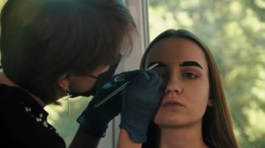 Genç kadın kozmetik uzmanı modelin kaşlarını koyu kahverengi renkle dolduruyor.
