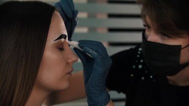 Koyu renk boyalı ve kaşlarını fırçayla fırçalayan genç bir kadının kaşlarını doldurmak.