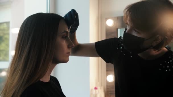 若い女性の美容師は、モデルの眉毛に白いマークアップを描画し、余分なものを一掃 — ストック動画