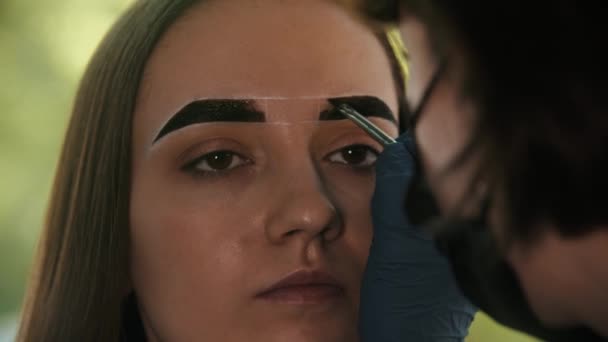 Cosmetologist jovem mulher preenche a sobrancelha do modelo com cor marrom escuro na frente — Vídeo de Stock