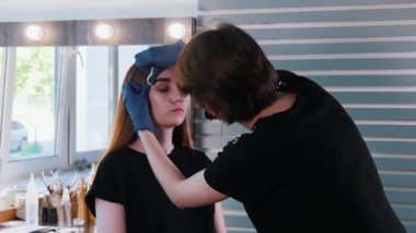 Kaş ustası, genç bayanın renkli kaşlarını fırçalıyor.