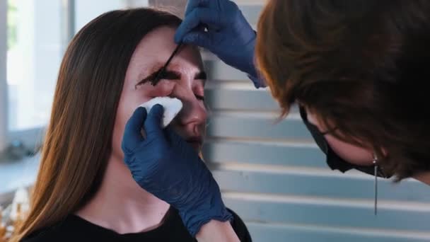 Brauenmaster bürstet und wischt die Augenbrauen-Haarfärbung mit einem Wattepad ab — Stockvideo
