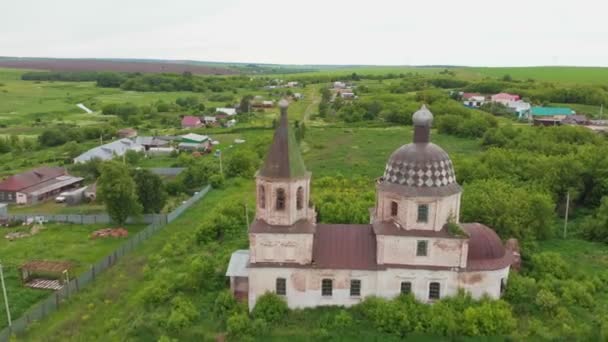 Старая церковь посреди зеленого поля с несколькими жилыми кварталами в деревне — стоковое видео