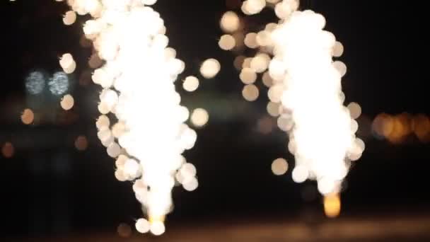 Dos pequeños fuegos artificiales blancos ardiendo y explotando - esparce destellos en la playa - desenfocados — Vídeo de stock