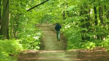 Yeşil ormanda kapüşonlu genç adam koşuyor.