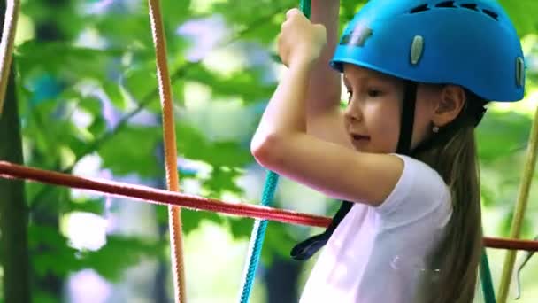 Seilabenteuer im Park - ein kleines Mädchen mit Helm bewegt sich über die Seilbrücke — Stockvideo