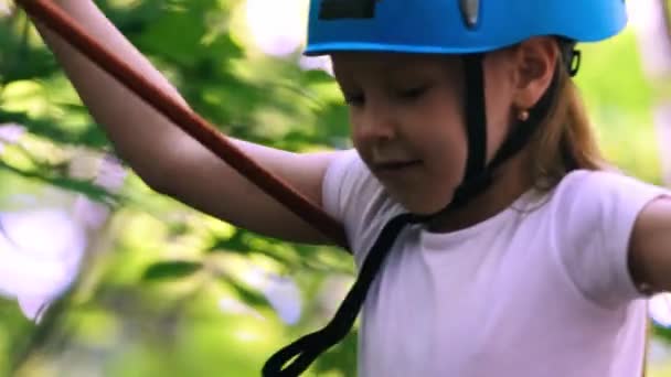 Seilabenteuer im Park - ein kleines Mädchen bewegt sich über die Seilbrücke und zieht den Haken an einem anderen Versicherungsseil aus — Stockvideo