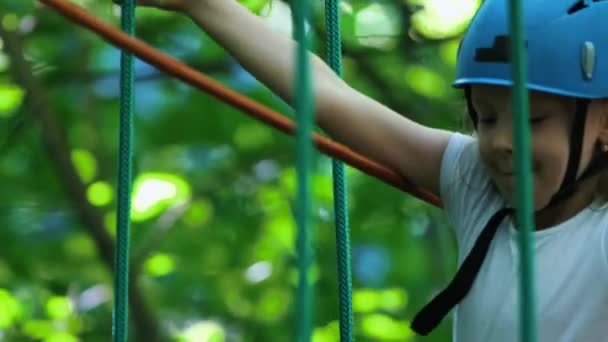 Touw avontuur in het park - een klein meisje in de helm bewegen over de touwbrug op hoog — Stockvideo