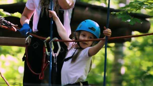 Extreme rope adventure in the park - a little girl in full protection moving over the rope bridge on high — Stock Video