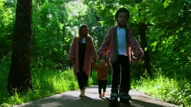 A szülők fiatal családja és a nyári parkban sétáló két kisgyerek - egy görkorcsolyázó lány — Stock videók