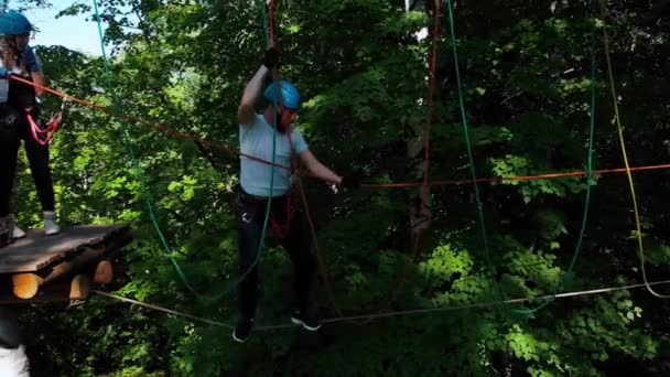 Экстремальное приключение на веревке в парке - мужчина и женщина, идущие по веревке между двумя стендами со страховкой — стоковое видео