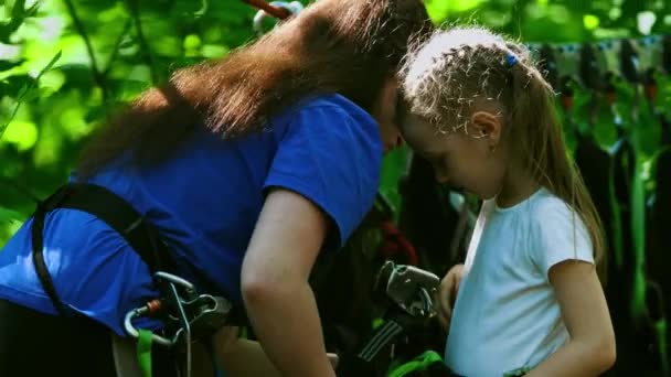 Rope adventure - μια γυναίκα εκπαιδευτής βάζει τα ασφαλιστικά μενταγιόν στη μέση ενός μικρού κοριτσιού — Αρχείο Βίντεο