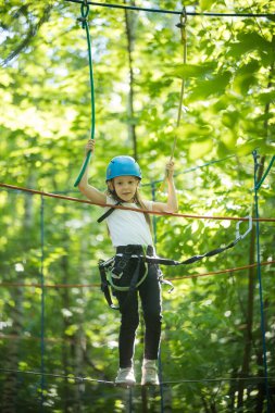 Ormanda bir halat macerası - küçük bir kız köprüde duruyor ve kameraya bakıyor.