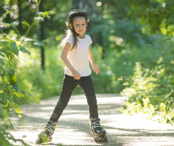 Una niña pequeña en casco protector patinando en el bosque en sus rodillos — Foto de Stock