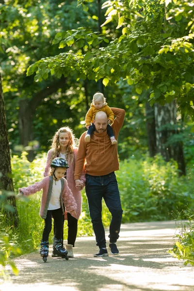 Familia joven de padres y dos niños pequeños caminando en el parque — Foto de Stock