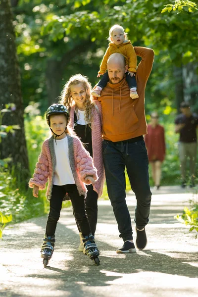 Joven familia feliz de padres y dos niños pequeños caminando en el bosque verde — Foto de Stock