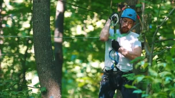 Mężczyzna w kasku przeżywający przygodę linową w lesie z pełnym ubezpieczeniem - schodzący z pasa ubezpieczeniowego — Wideo stockowe