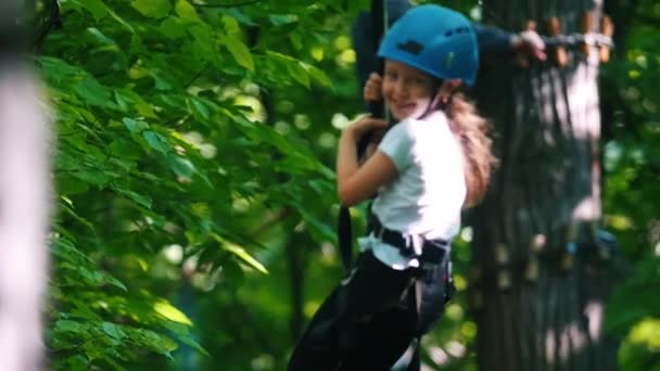 Egy kislány lóg a biztosítási kábelen az öve - kötél híd szórakoztató attrakció — Stock videók