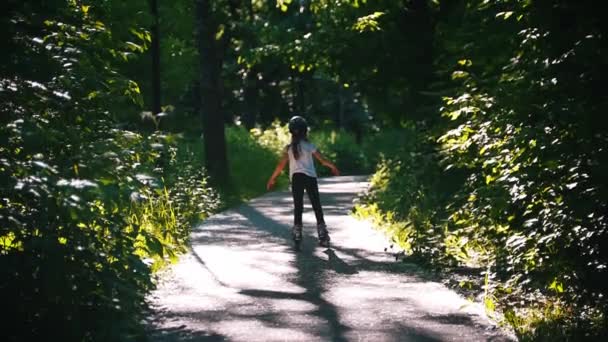 Una chica en el casco patinando en el bosque en sus rodillos — Vídeos de Stock