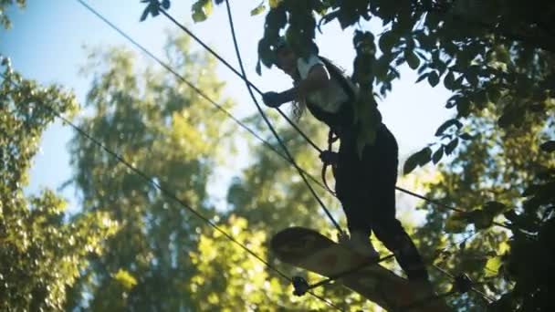 Mulher que tem uma atração de entretenimento na floresta verde - cruzando a construção da corda usando um skate — Vídeo de Stock