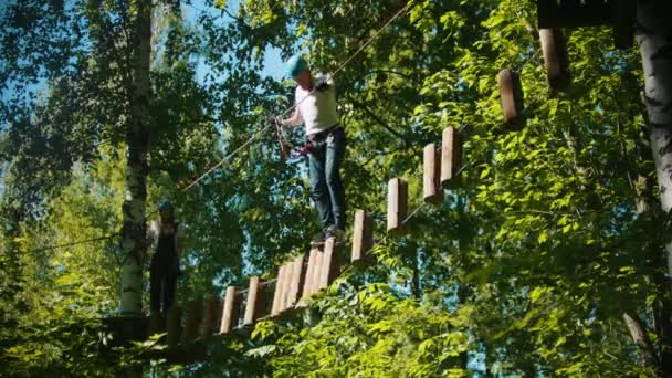 Uomo e donna che attraversano una costruzione della corda e ceppi - un'attrazione di intrattenimento nella foresta verde — Video Stock
