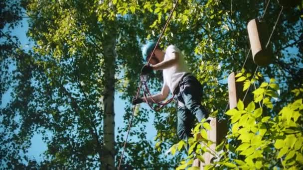 Mann überquert eine Konstruktion aus Seil und Baumstümpfen und hält sich am Versicherungsseil fest - eine Attraktion im grünen Wald — Stockvideo