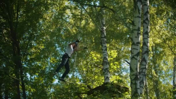 Uomo in piena assicurazione che attraversa la corda da un albero all'altro - un'attrazione di intrattenimento nella foresta — Video Stock