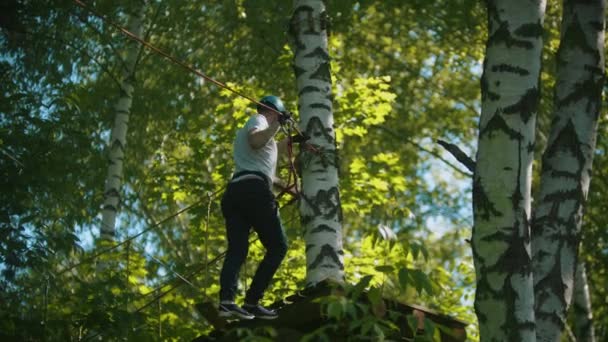 Mann in Vollkasko überquert Seil auf dem Weg zum Stand - eine Attraktion im Wald — Stockvideo