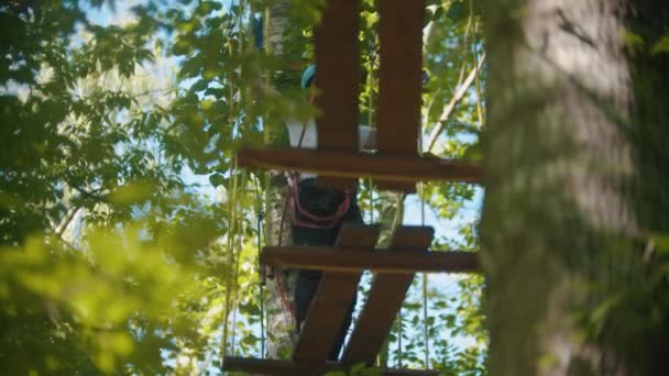 Mulher em seguro completo cruzando a ponte de corda - uma atração de entretenimento na floresta — Vídeo de Stock