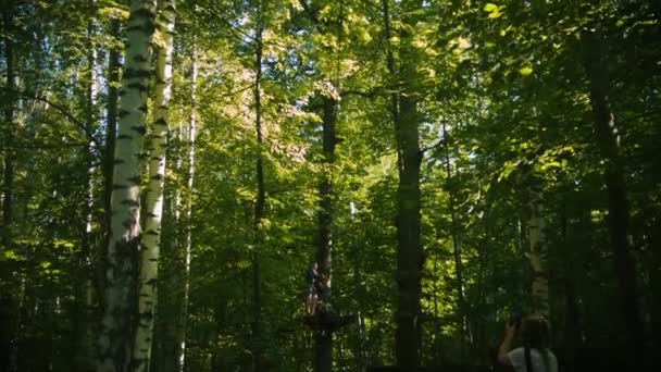 Eine Frau fotografiert ihre kleine Tochter, die am Versicherungsgürtel im Wald hängt - ein Vergnügen im Freizeitpark — Stockvideo