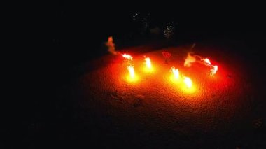 Kumsalda havai fişekler yanıyor. Kırmızı havai fişekler dönüyor ve etrafa yayılıyor.