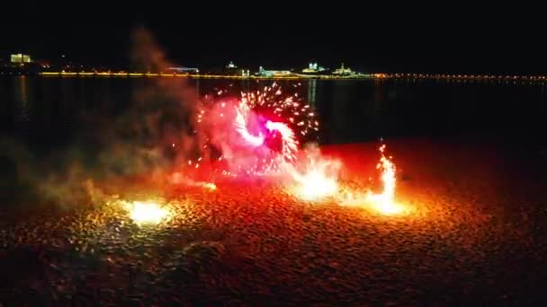 Bir gece şehrinin plajında havai fişekler yanıyor. Kırmızı havai fişekler dönüyor ve etrafa ışıldıyor. — Stok video