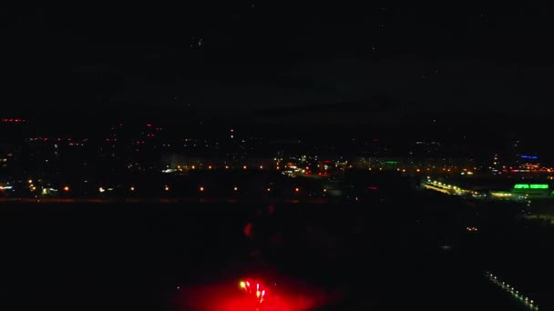 Hermosos fuegos artificiales brillantes que explotan en el aire sobre un fondo del río y la ciudad nocturna — Vídeos de Stock