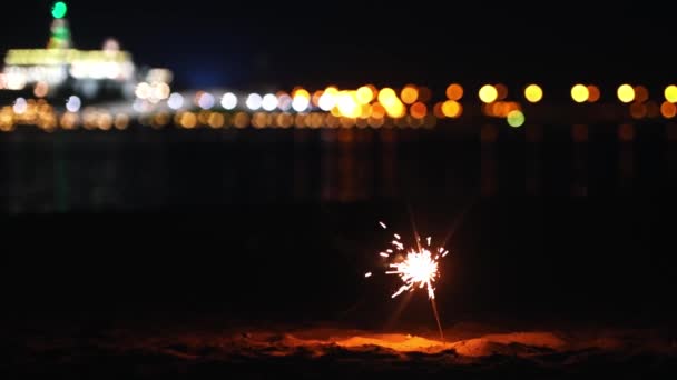 Bruciante scintillante nella sabbia sulla spiaggia della città di notte — Video Stock